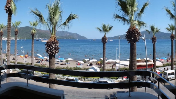 Un balcon avec vue sur une plage, des palmiers et des bateaux sur l’eau.
