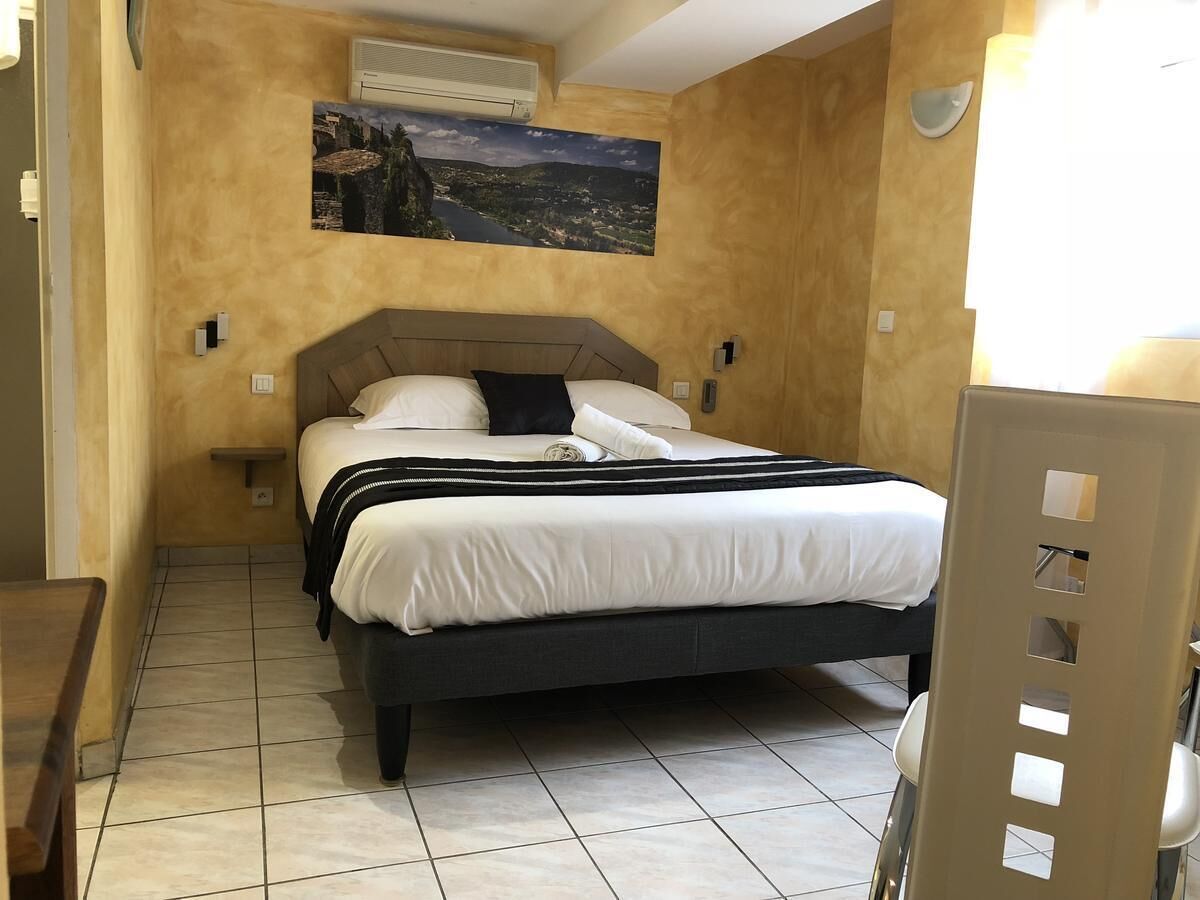 Um quarto com cama, mesa de cabeceira, cadeira, quadro na parede e janela.