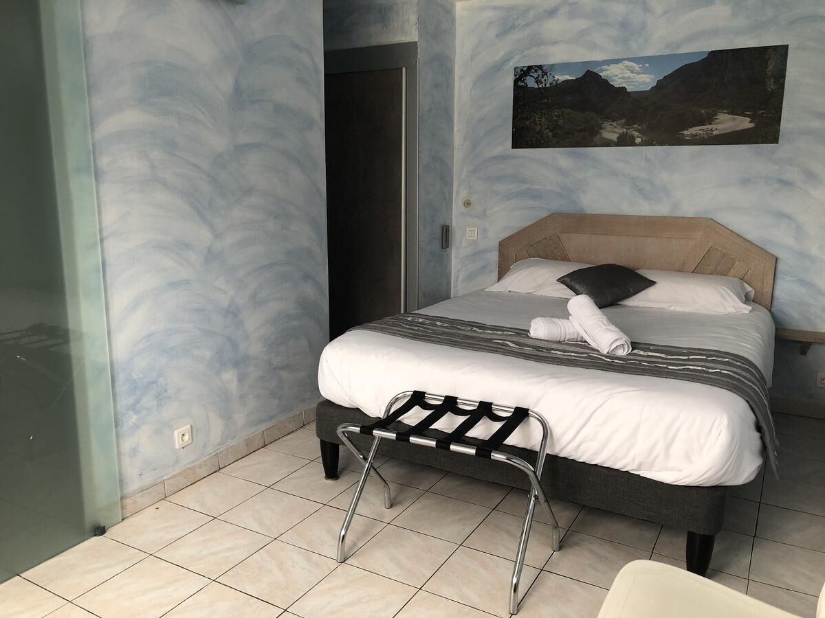 Quarto com cama, um pequeno banco, uma porta e um quadro pendurado na parede.