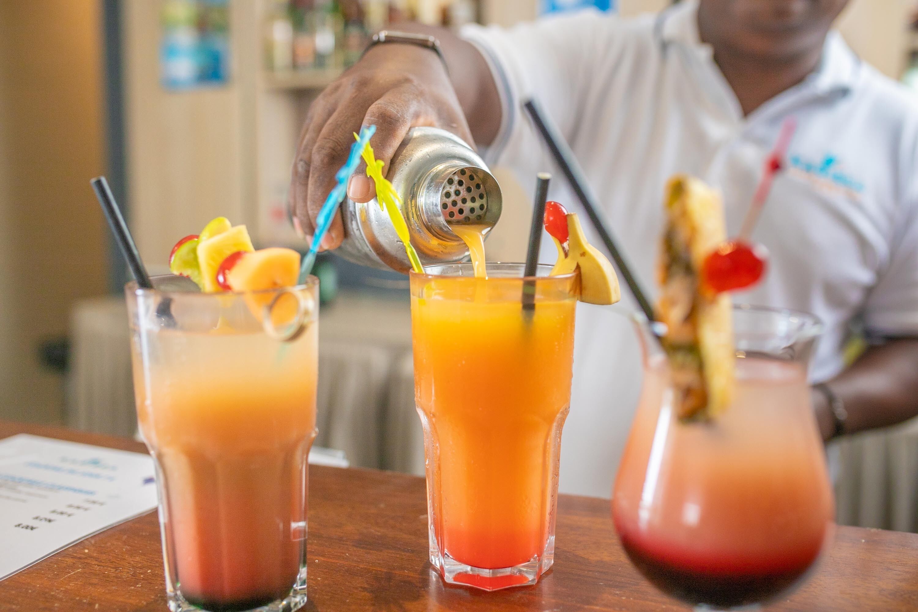 A bartender pouring a drink into a glass with fruit garnishes.