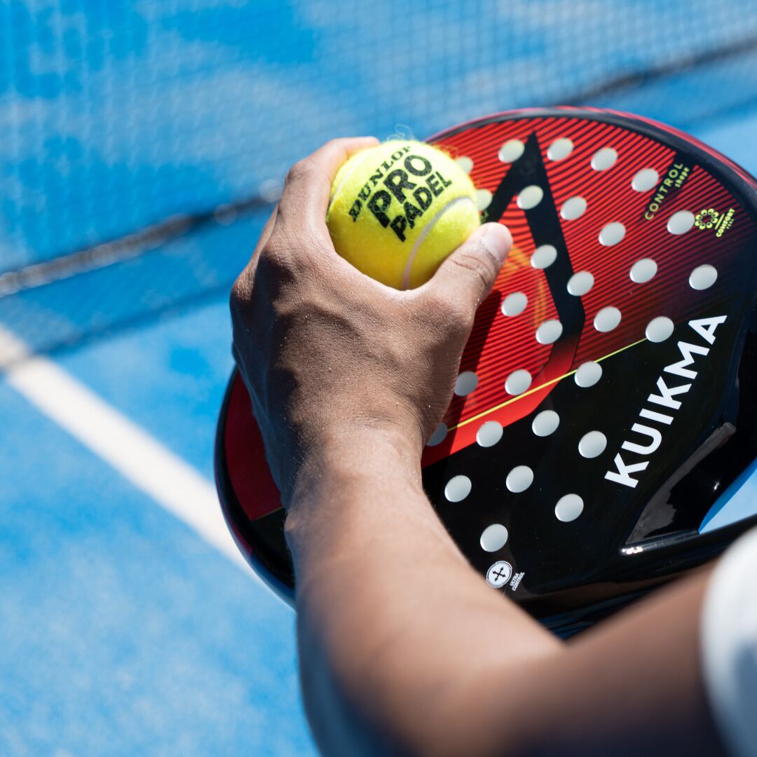 A hand holding a tennis ball and racket with "PENTUP PRO PADEL" and "KUIKMA" visible.