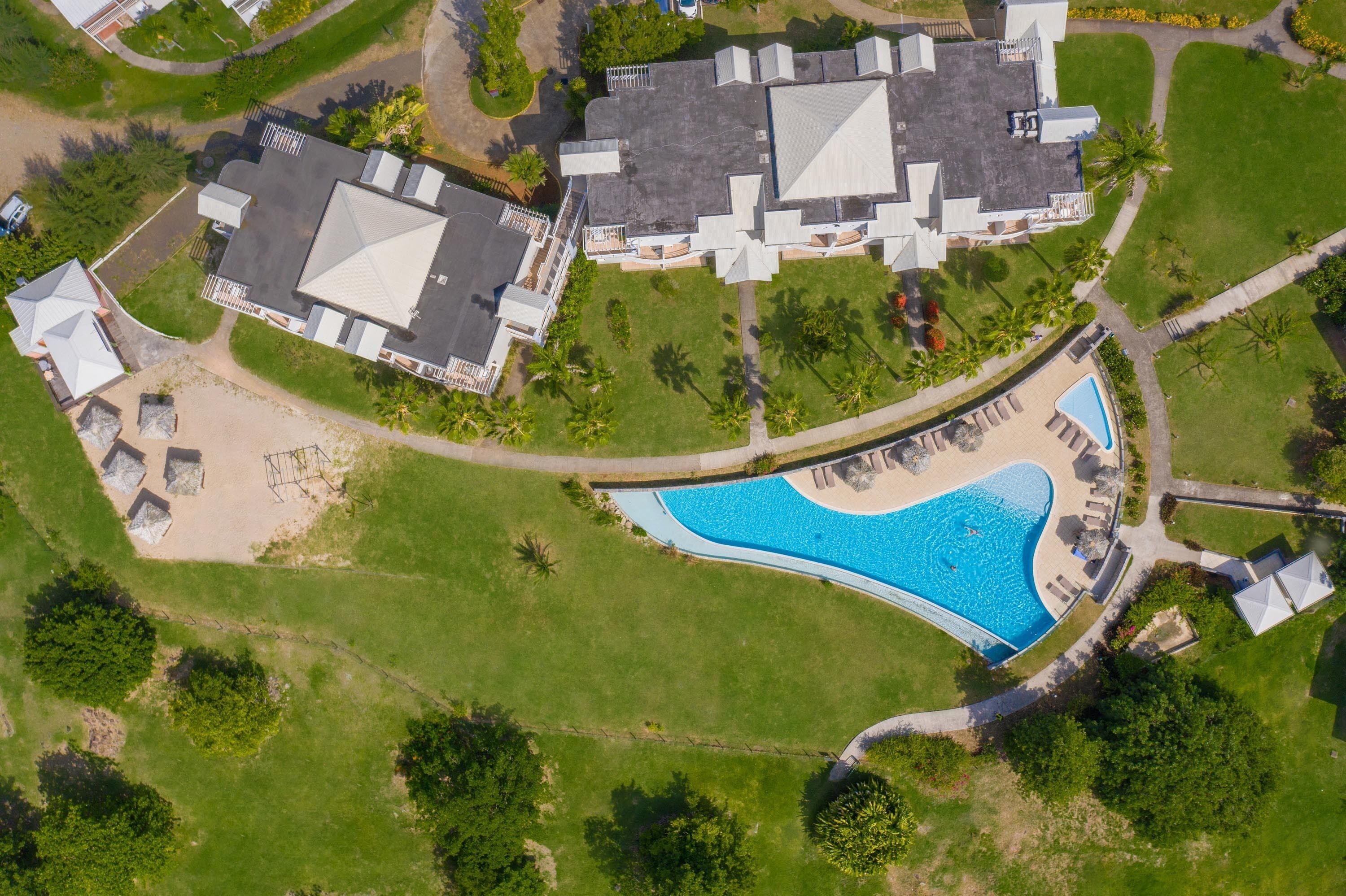 Vista aérea de una zona residencial con piscina, varias casas y céspedes bien cuidados.