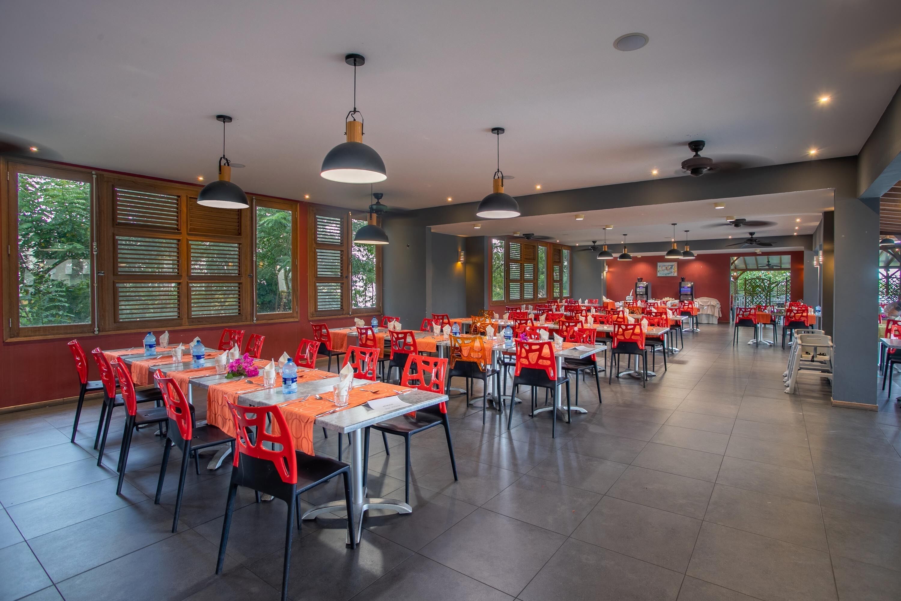A spacious dining area with multiple tables and chairs, large windows, and pendant lighting.