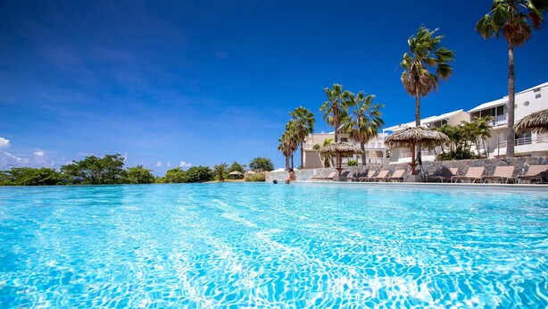A clear blue pool with lounge chairs and palm trees, surrounded by a resort building. - Karibea Sainte Luce hotel (Sainte-Luce)