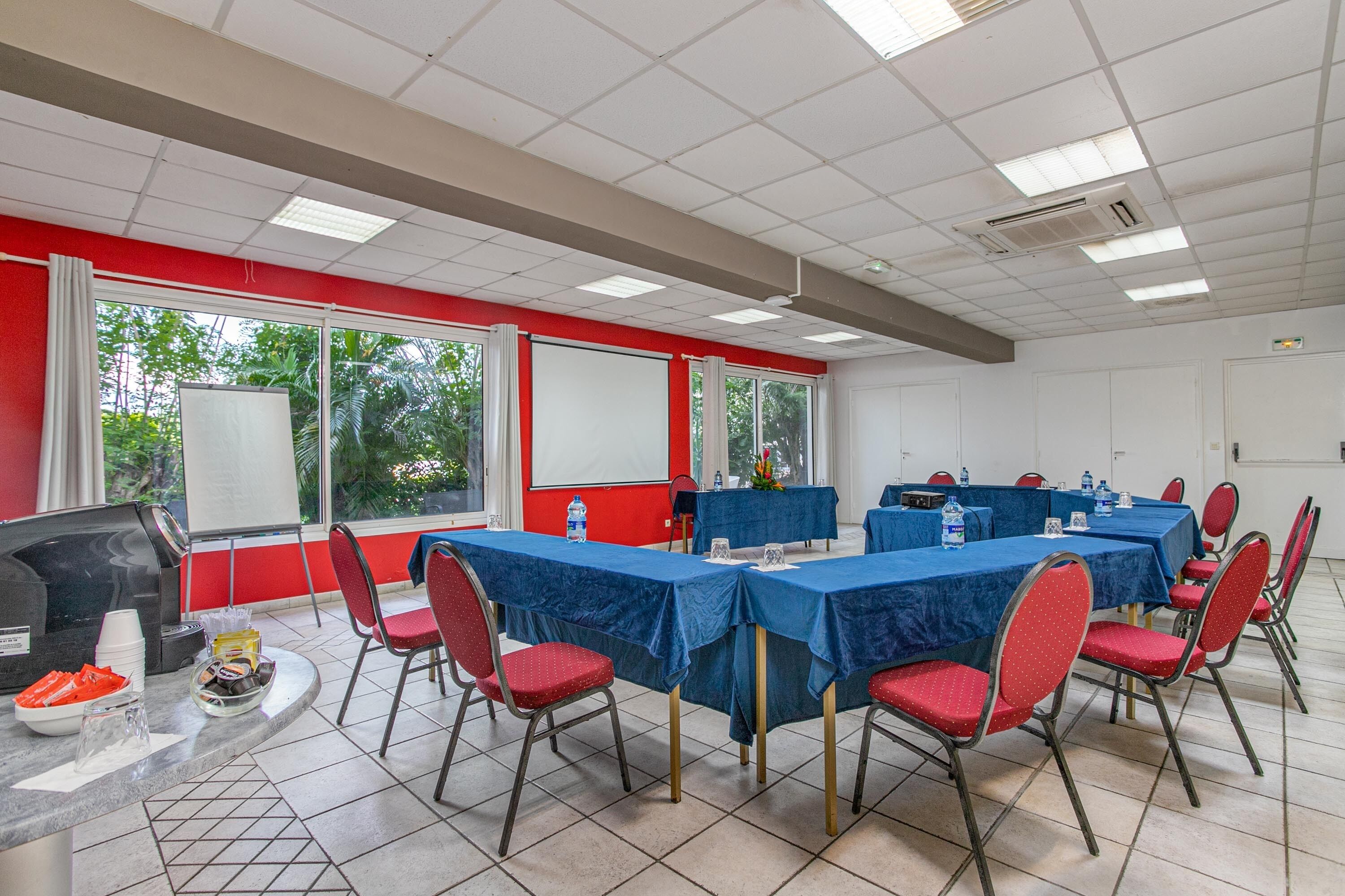 Una sala de conferencias con mesas, sillas, un proyector y una pantalla.