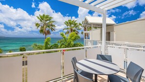 A balcony with a table and chairs, overlooking a beach with palm trees and the ocean. - Karibea Sainte Luce hotel (Sainte-Luce)