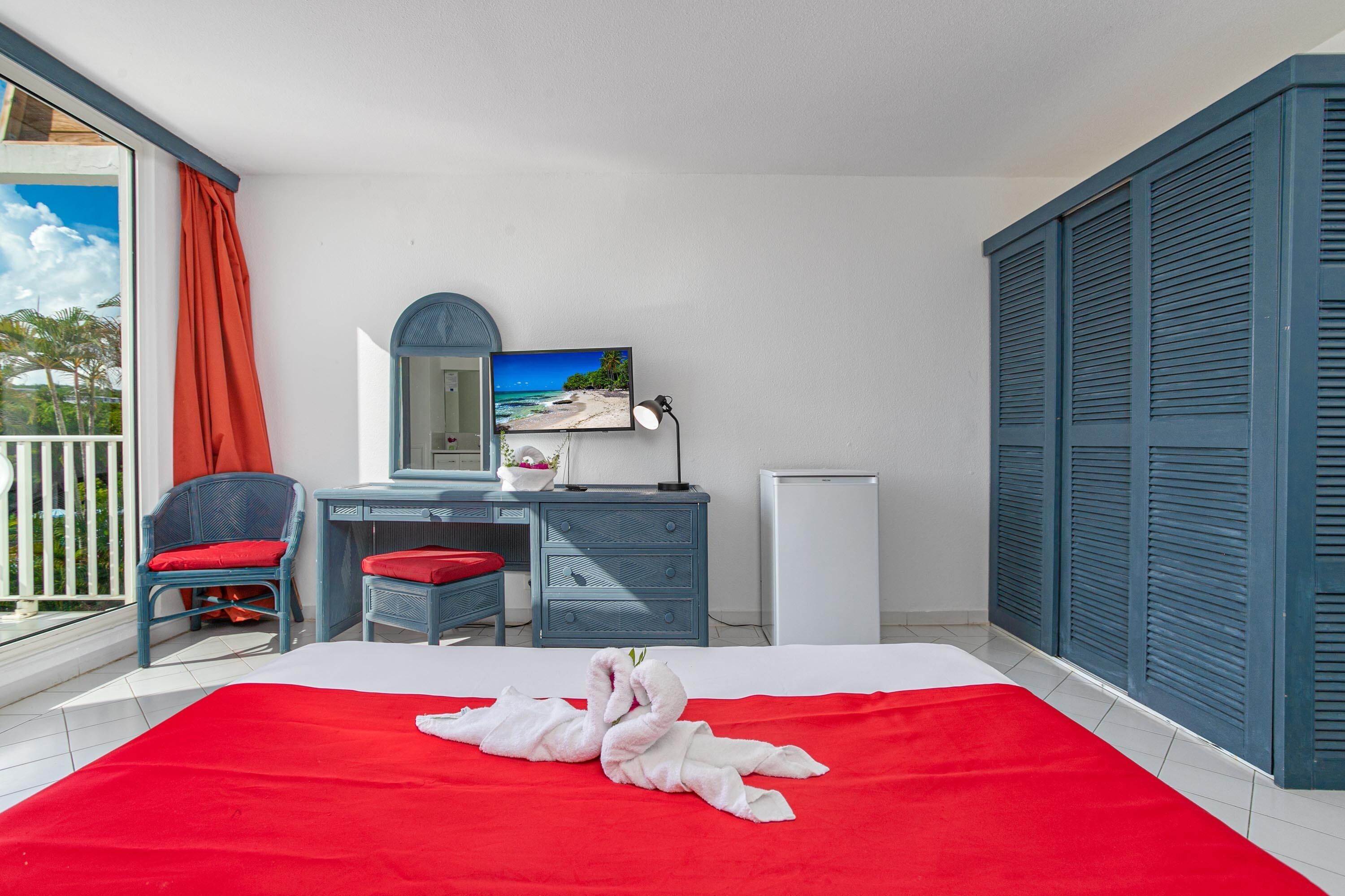 A hotel room with a bed, a desk, a chair, a TV, and a balcony.