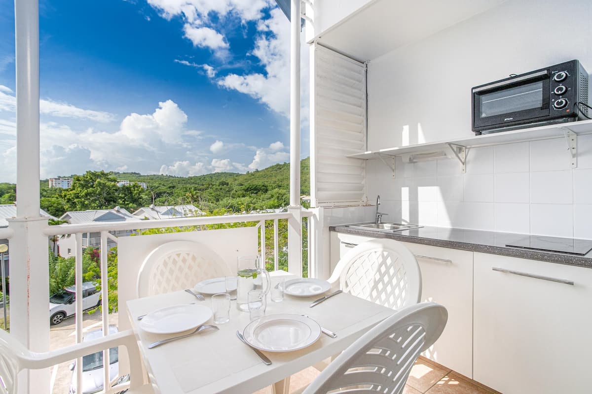 A balcony with a dining table set for two, a microwave, and a view of a green landscape.
