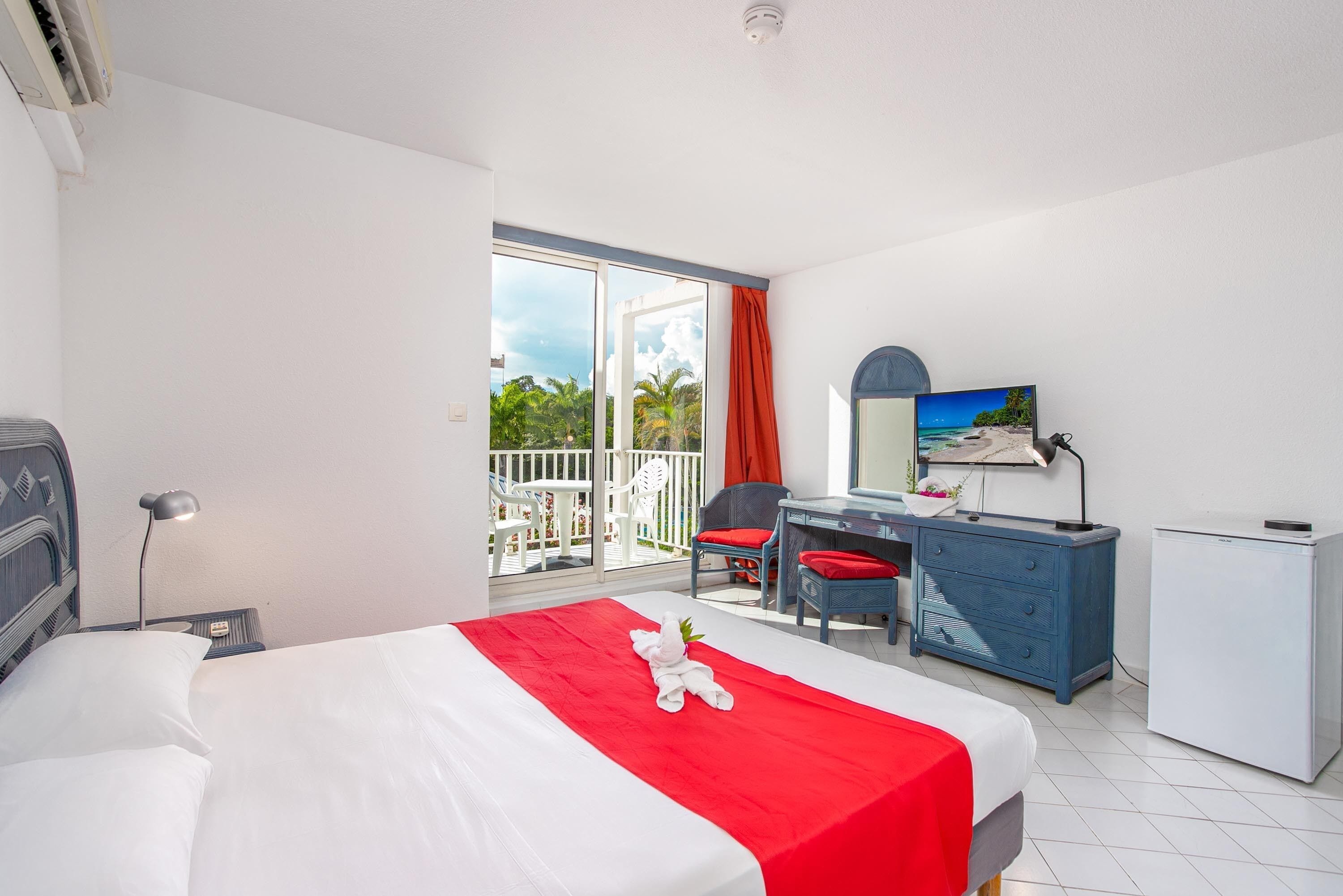 A hotel room with a bed, desk, chair, and a small refrigerator.