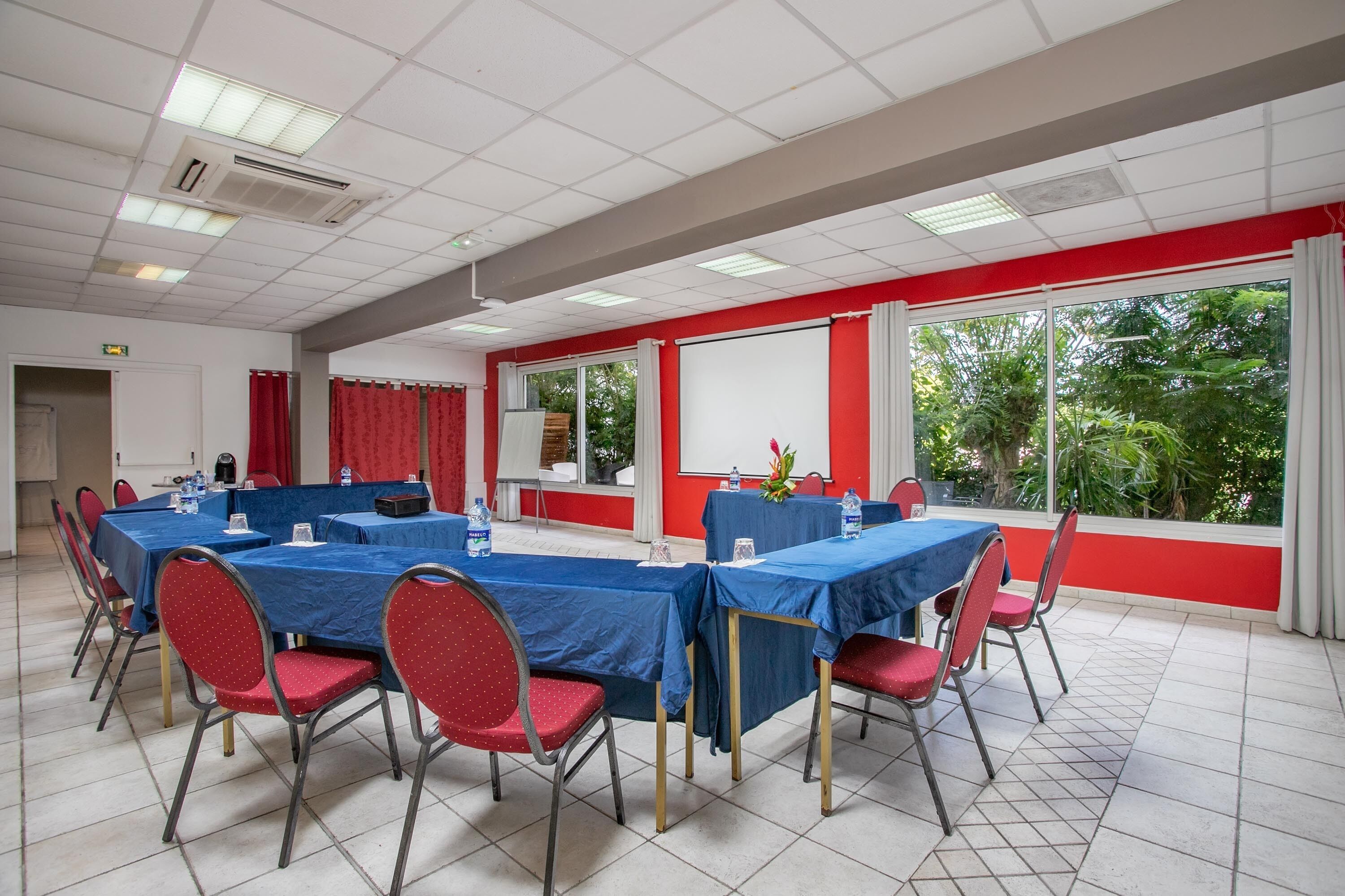 A conference room with tables and chairs, large windows, and a projector screen.