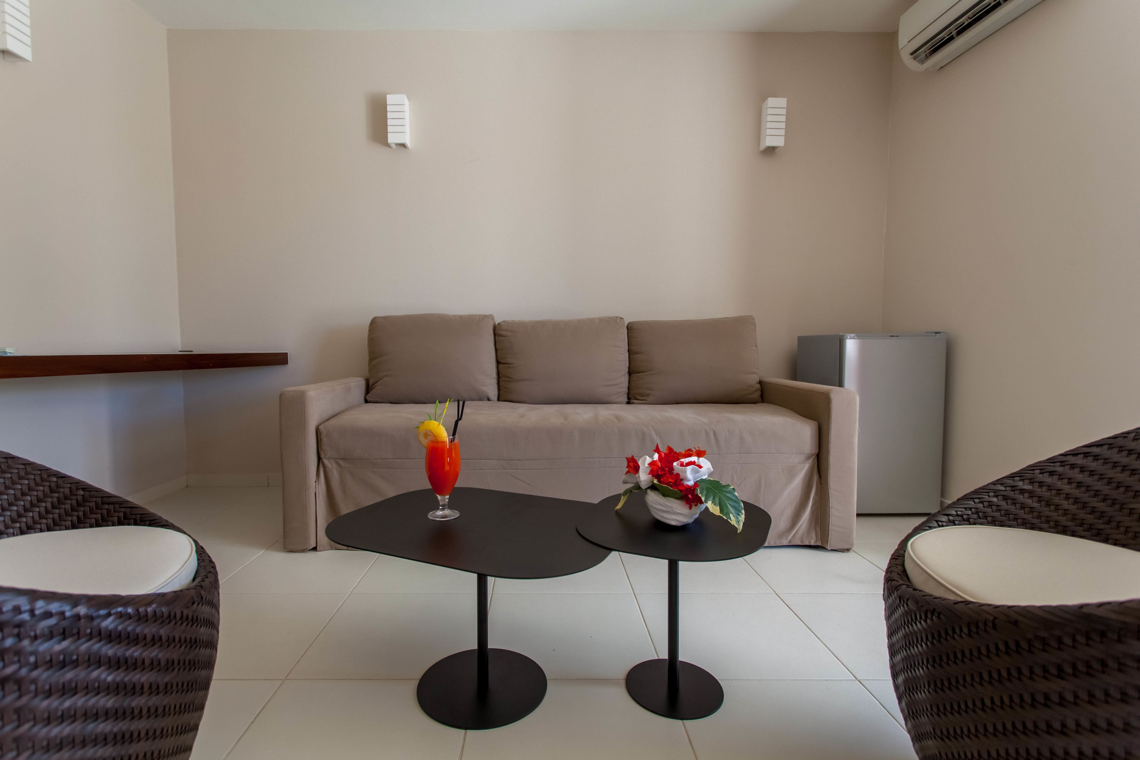 A modern living room with a sofa, two black tables, wicker chairs, and a refrigerator.
