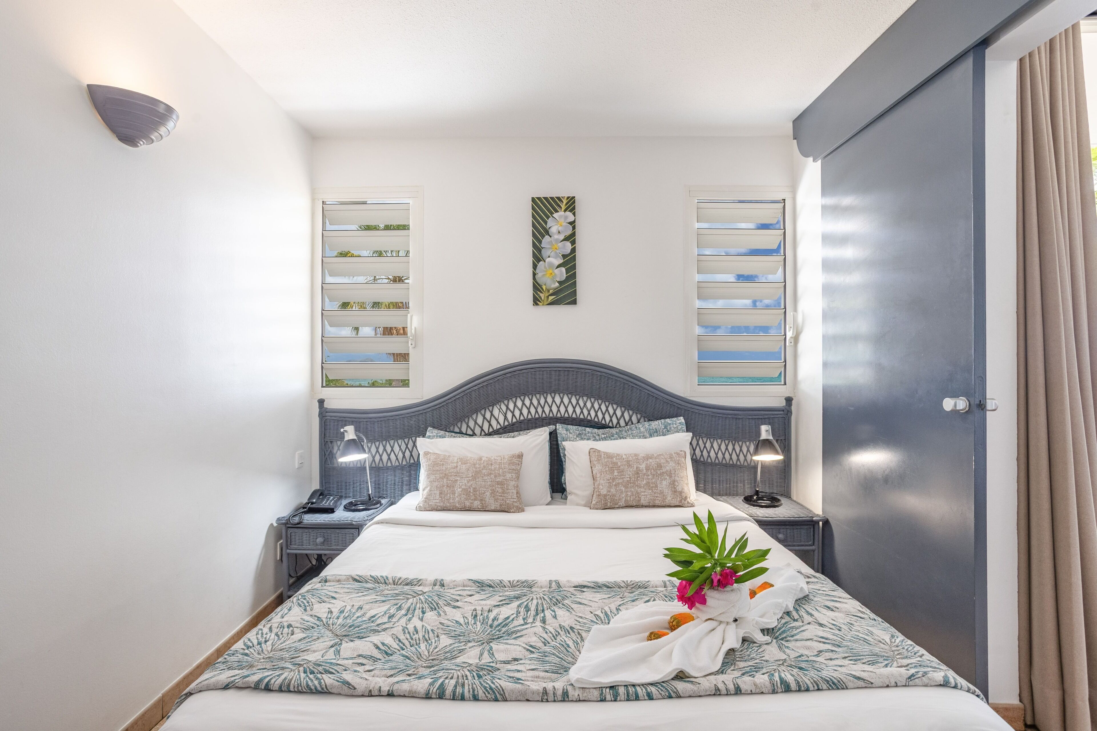 A neatly arranged hotel room with a bed, bedside tables, a wall-mounted shelf, and a door.