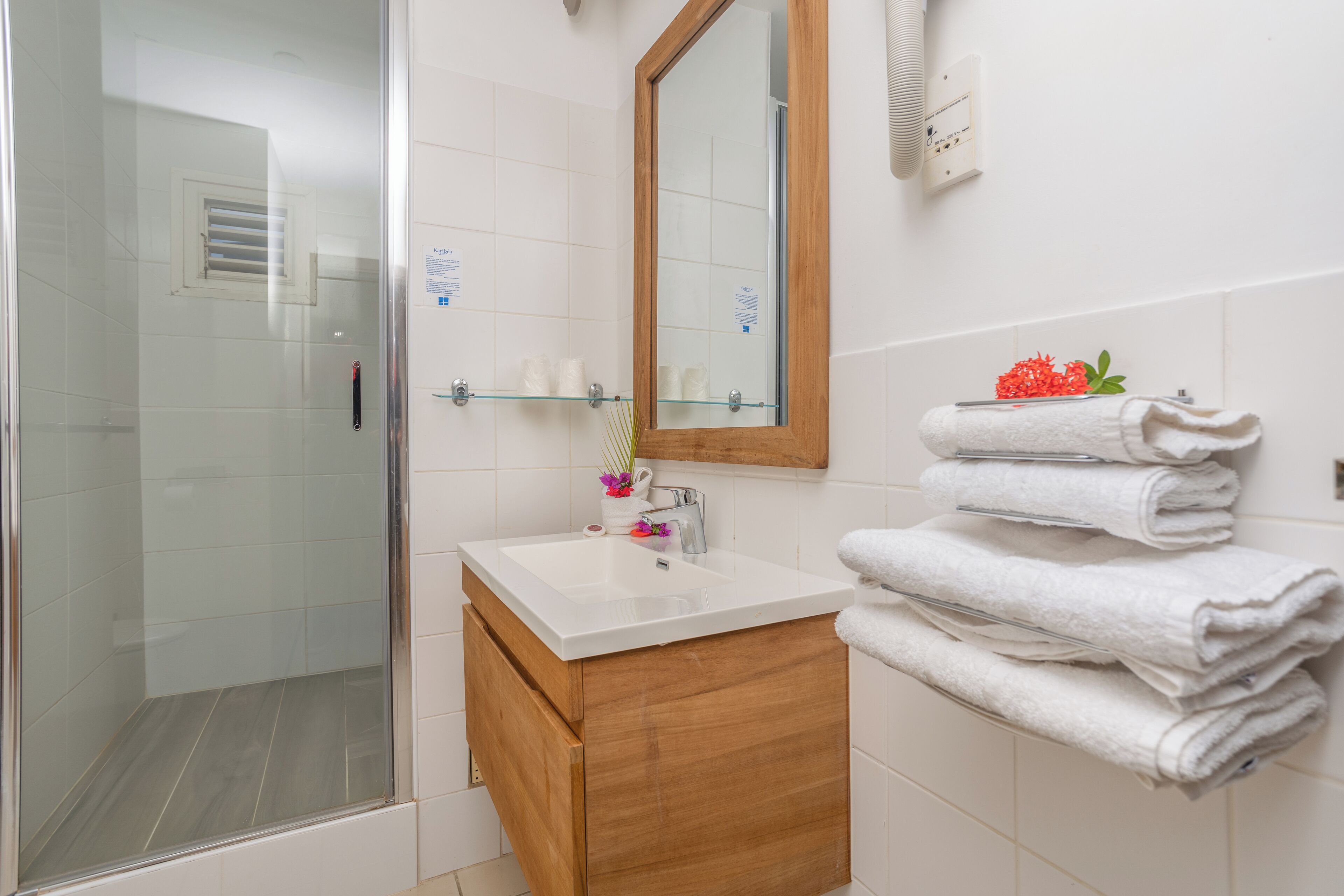 Un baño con cabina de ducha de vidrio, un lavabo blanco, un tocador de madera y un espejo.