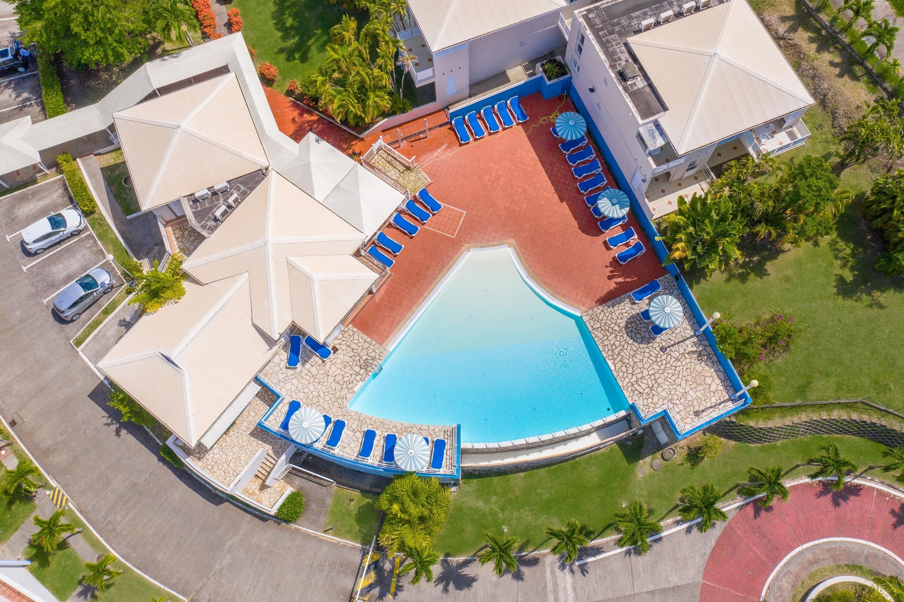 Vue aérienne d’un complexe hôtelier doté d’une piscine, de plusieurs espaces de détente et d’un parking.
