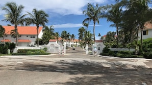 A gated entrance with palm trees and buildings with red roofs. - Delaporte Point Oceanfront Townhouse (Nassau)
