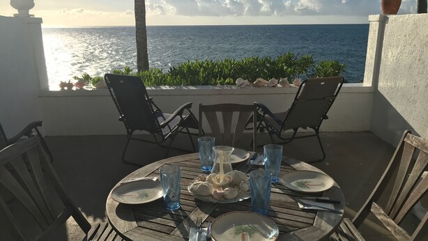 A round wooden table set for two with plates, glasses, and cutlery, overlooking the sea. - Delaporte Point Oceanfront Townhouse (Nassau)