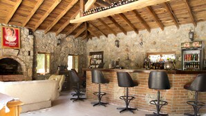 A rustic bar area with stone walls, wooden ceiling beams, and a brick fireplace. There are bar stools and a bookshelf with various items. - Doga Apartments (Fethiye)
