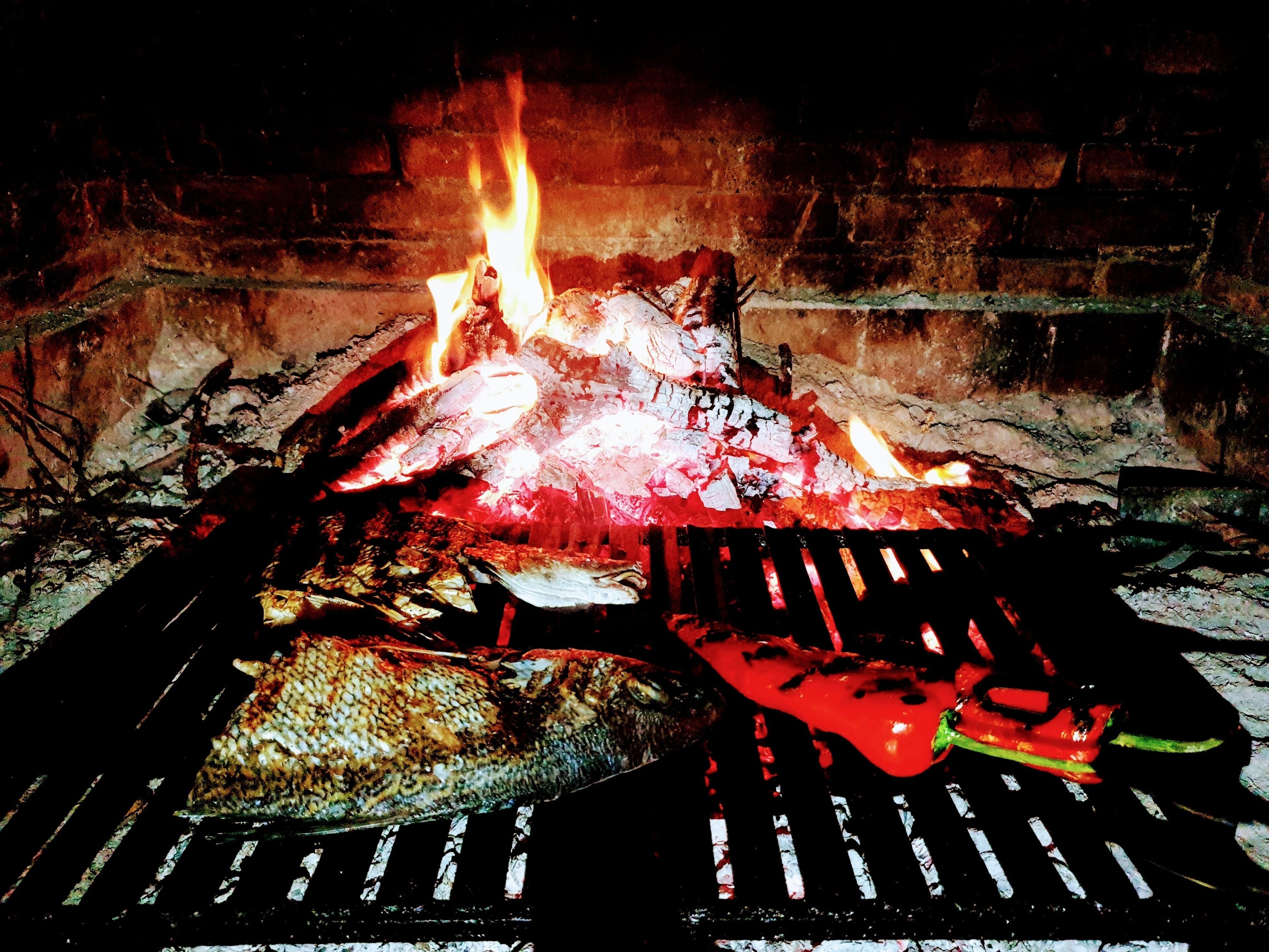 A grill with food and a fire in the background.