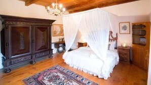 Een slaapkamer met een houten plafond, een hemelbed, een grote houten garderobe en een kamerkleed met een patroon.