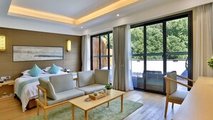 A modern hotel room with a bed, sofa, armchair, and a dining table. There is a large window with a view of greenery outside. - Hiking Hotel Hangzhou (Hangzhou)