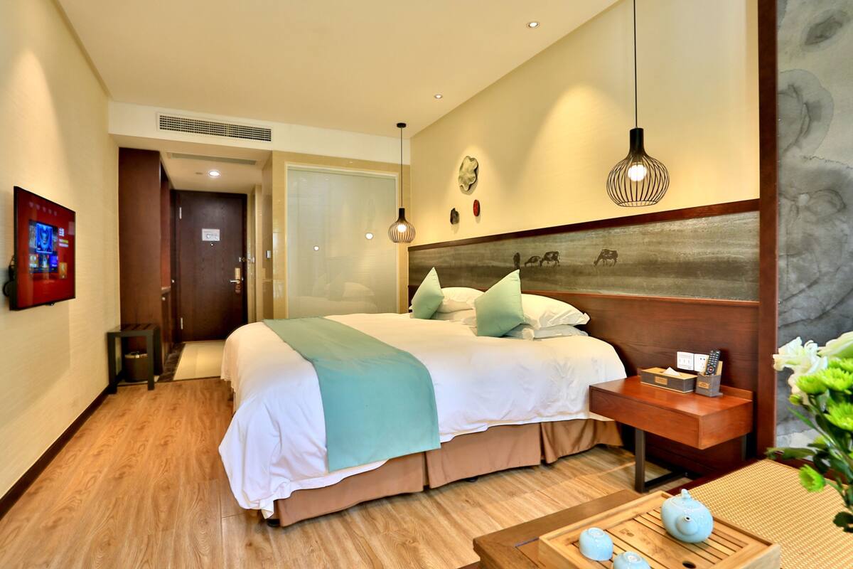 A hotel room with a large bed, bedside table, and a small table with teapots.