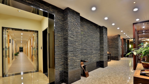 A modern hotel lobby with a long corridor, a stone wall, and a reception area with a plant and a table. - Hiking Hotel Hangzhou (Hangzhou)