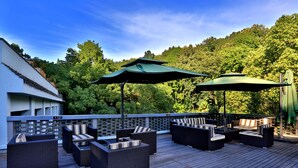 An outdoor deck with wicker furniture and green umbrellas, surrounded by lush greenery. - Hiking Hotel Hangzhou (Hangzhou)