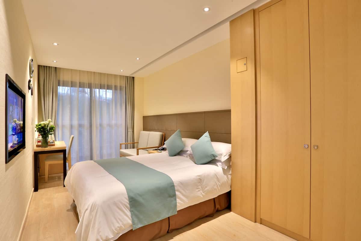 A hotel room with a large bed, a desk with a chair, a television, and a wardrobe.