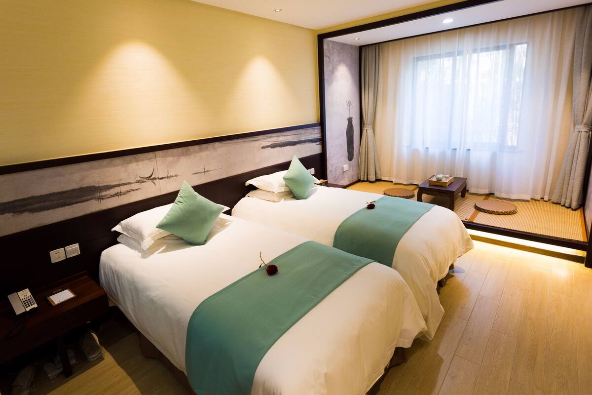 A hotel room with two beds, a small table, and a window with curtains.