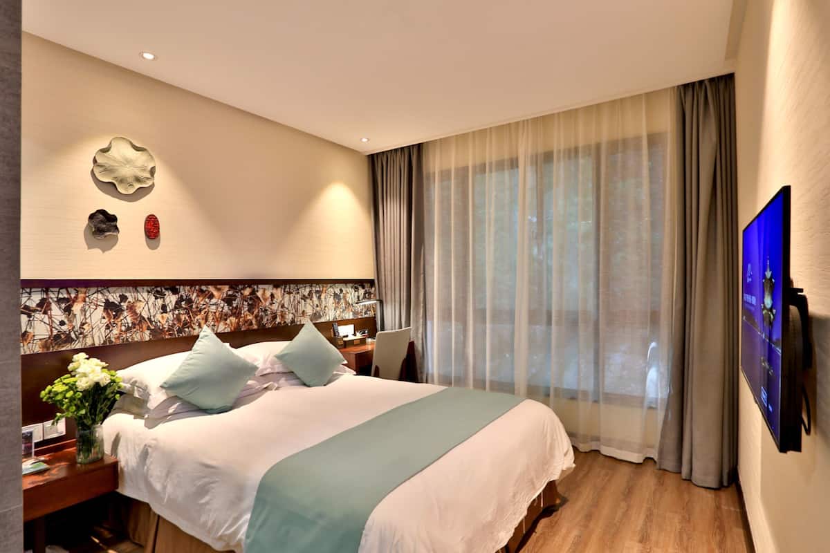 A hotel room with a large bed, a desk, a TV, and a window with curtains.
