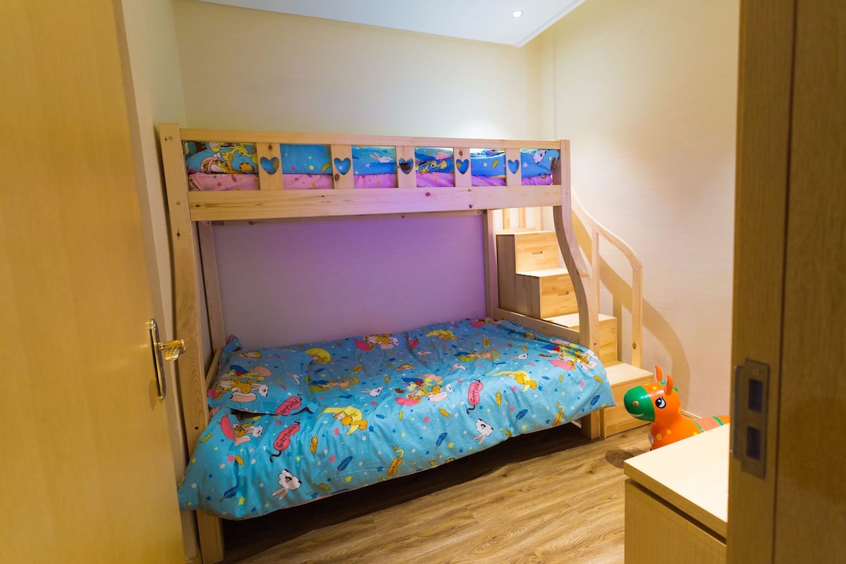 A bunk bed with a blue mattress featuring cartoon characters, a wooden headboard, and a small desk with a toy horse.