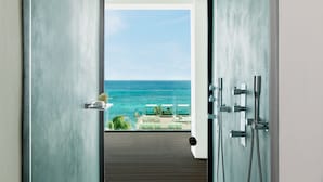 Un baño moderno con ducha, una puerta de cristal que da a un balcón con vistas al océano.