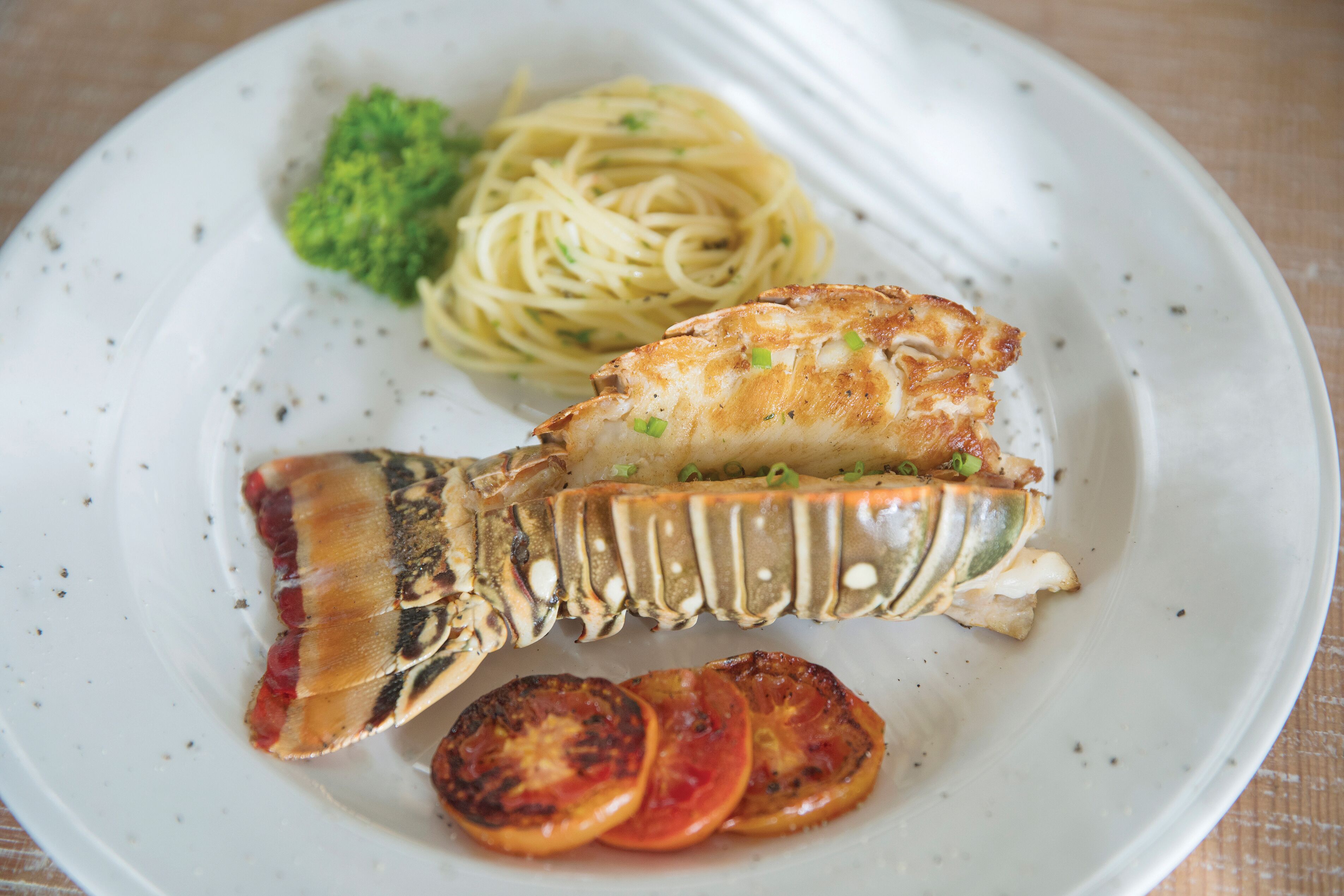 A plate with a grilled fish, pasta, broccoli, and grilled tomatoes.