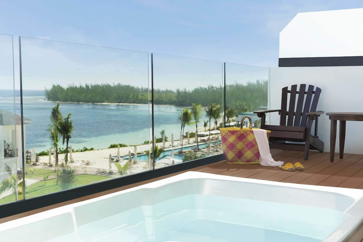 Ein Balkon mit Glasgeländer, einem Whirlpool, einem Holzstuhl und einem kleinen Tisch.