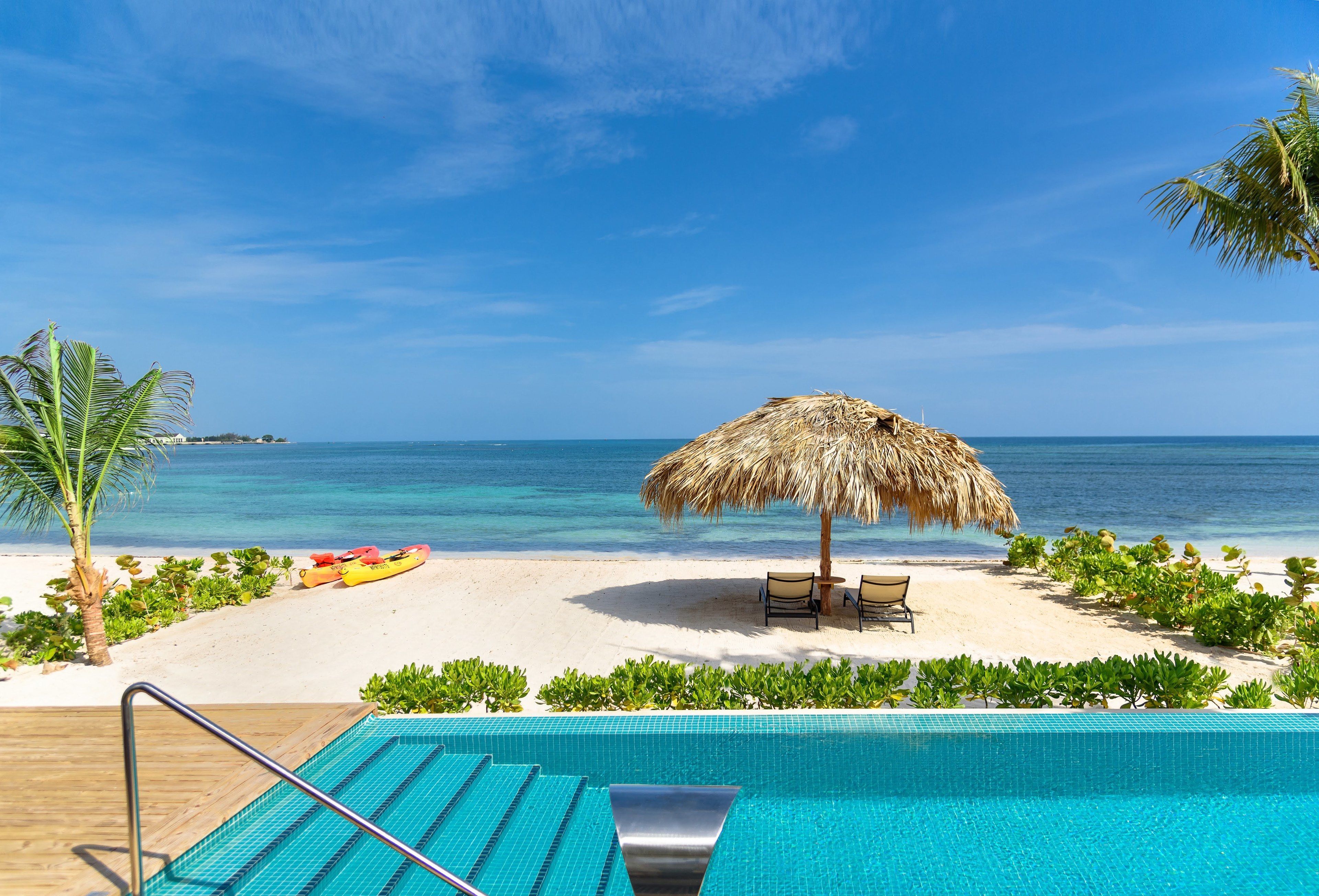 A poolside view with a beach and ocean in the background.