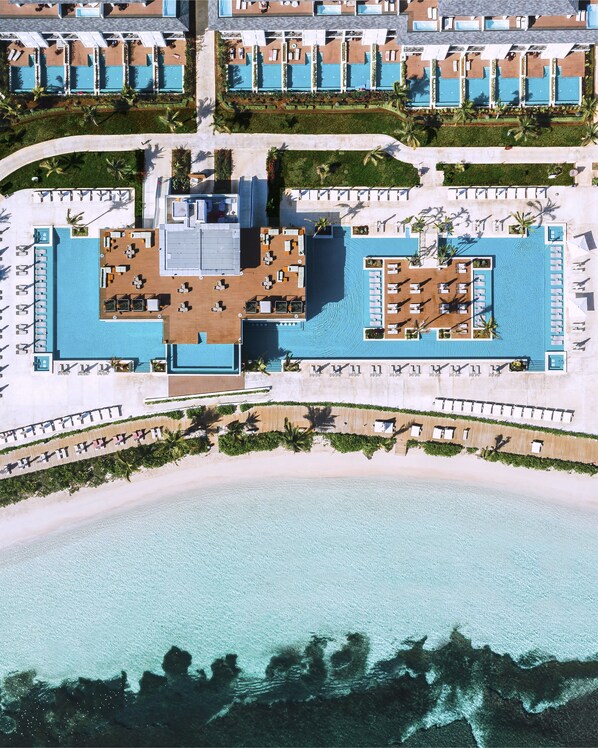 An aerial view of a resort with multiple swimming pools, sun loungers, and a beach area.