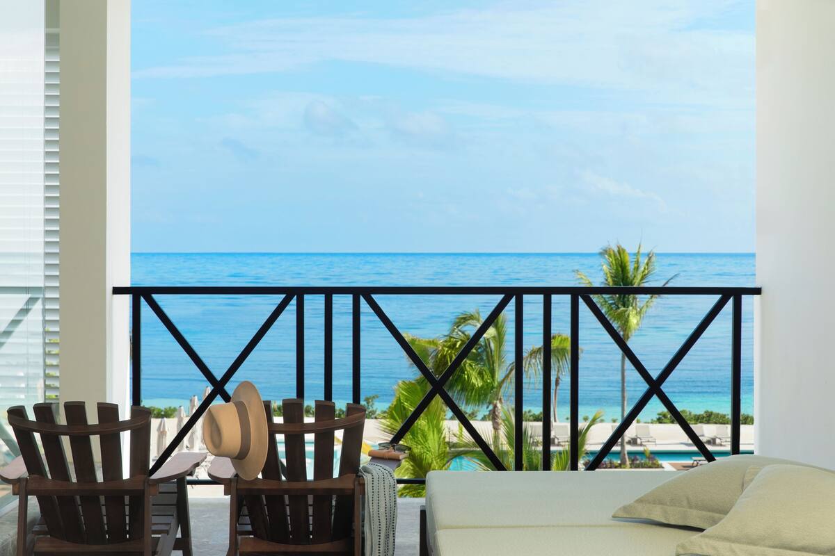 Ein Balkon mit Blick auf das Meer, Holzstühle, ein Hut und ein Pool.