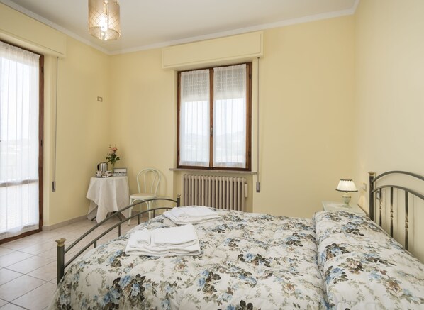 A bedroom with a bed, a chair, a table with a radio, and a window with curtains.