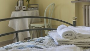 A neatly made bed with a floral bedspread, a metal headboard, and a stack of white towels. - Camere Mariella (Assisi)