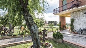 A courtyard with a tree, potted plants, and a brick building with a balcony. - Camere Mariella (Assisi)