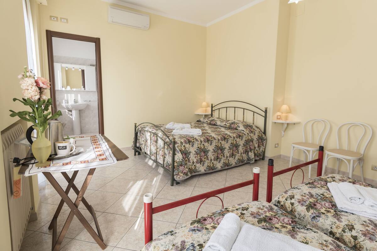 A bedroom with a bed, bedside tables, a small table with a vase and a cup, and a mirror.