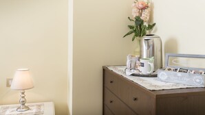 A neatly arranged desk with a lamp, a vase with flowers, a coffee maker, and a framed photo. - Camere Mariella (Assisi)