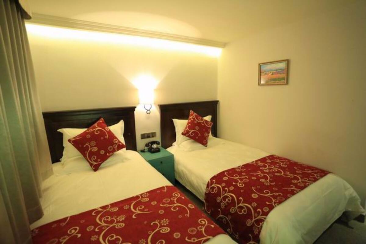 A hotel room with two beds, each with red and white bedding, a nightstand with a telephone, and a wall-mounted light fixture.