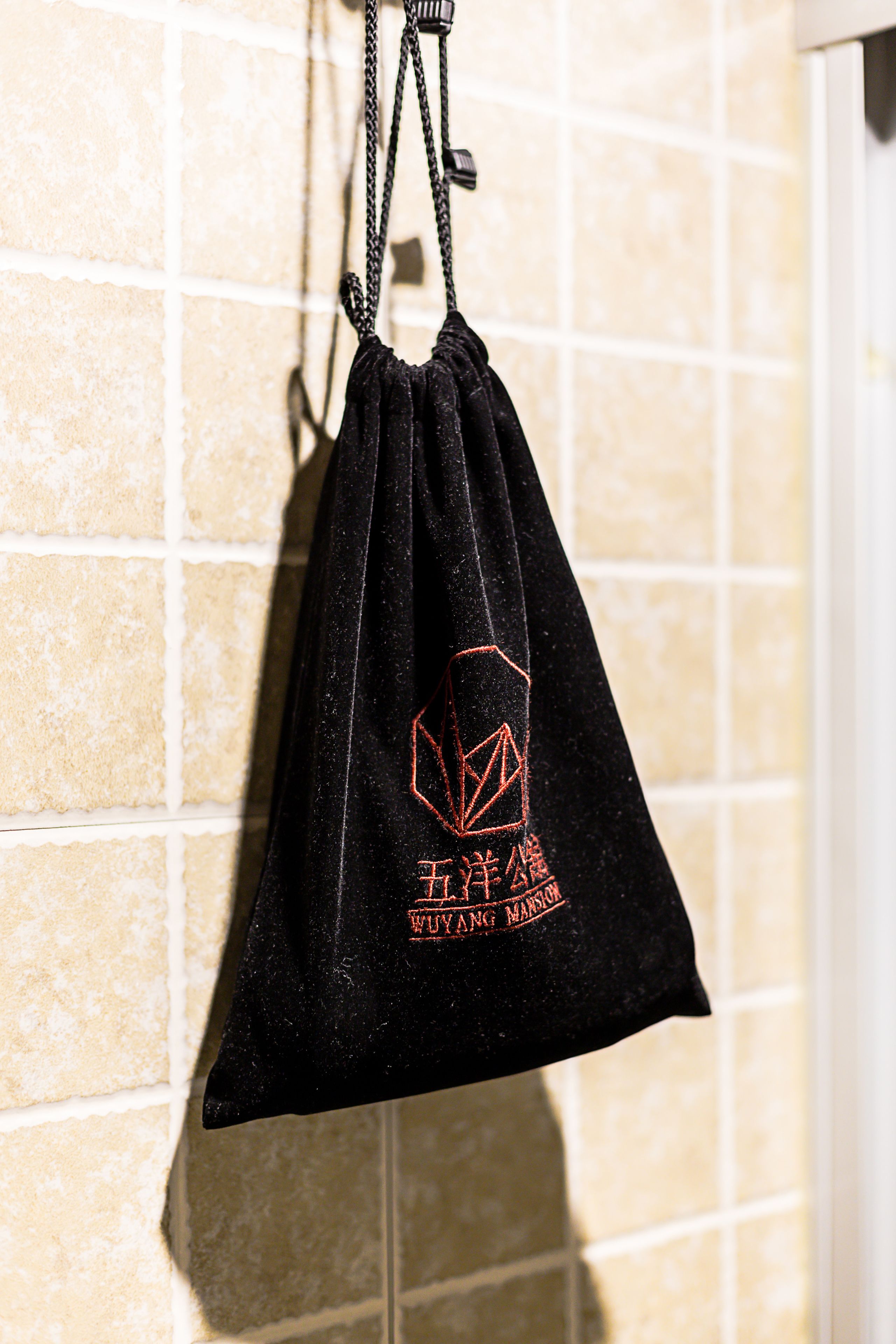 A black drawstring bag hanging on a tiled wall.