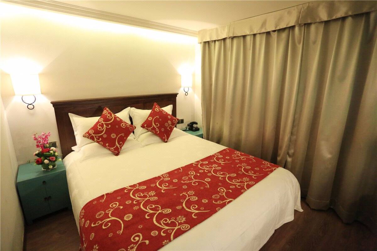 A hotel room with a large bed, two bedside tables, a nightstand, a lamp, and a curtain.