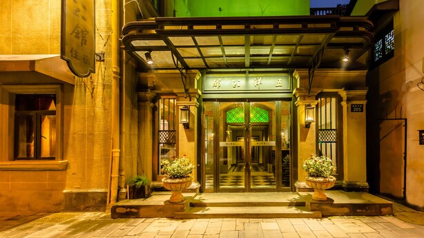 A hotel entrance with a green awning, a glass door entrance, and potted plants at the entrance.