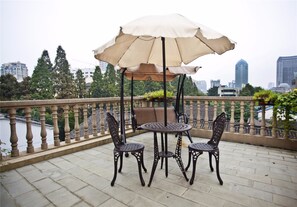 Ein Balkon mit Tisch, Stühlen und Sonnenschirm, mit Blick auf die Stadt.