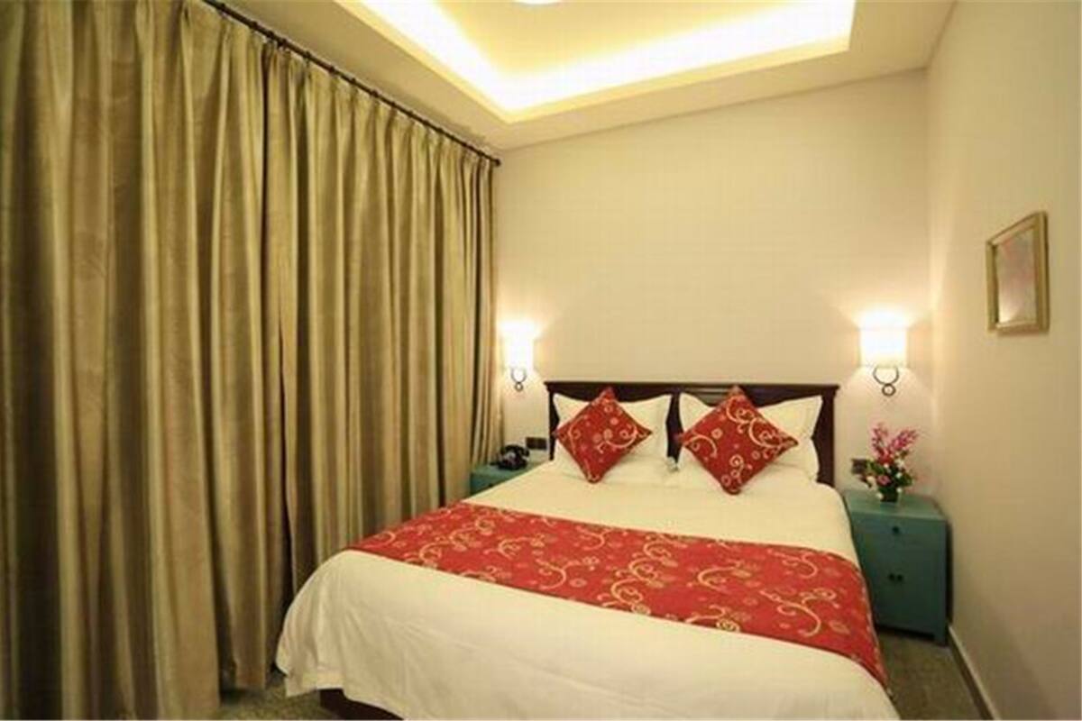 A hotel room with a bed, curtains, bedside lamps, and a nightstand with a vase.