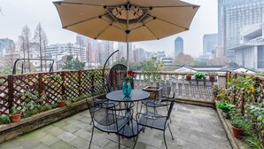 A rooftop terrace with a table and chairs, surrounded by potted plants and a large umbrella.