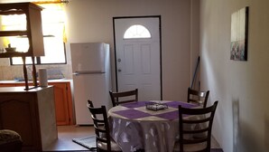 A dining area with a round table, four chairs, and a purple tablecloth. There is a white refrigerator and a door with a window in the background.